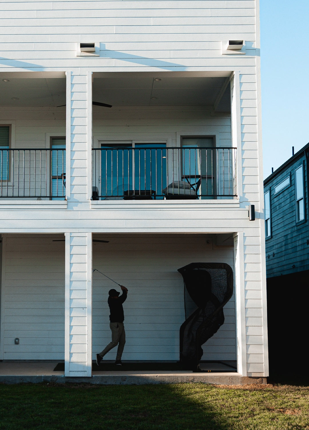 Person practicing golf swing in a white, two-story building with a net.