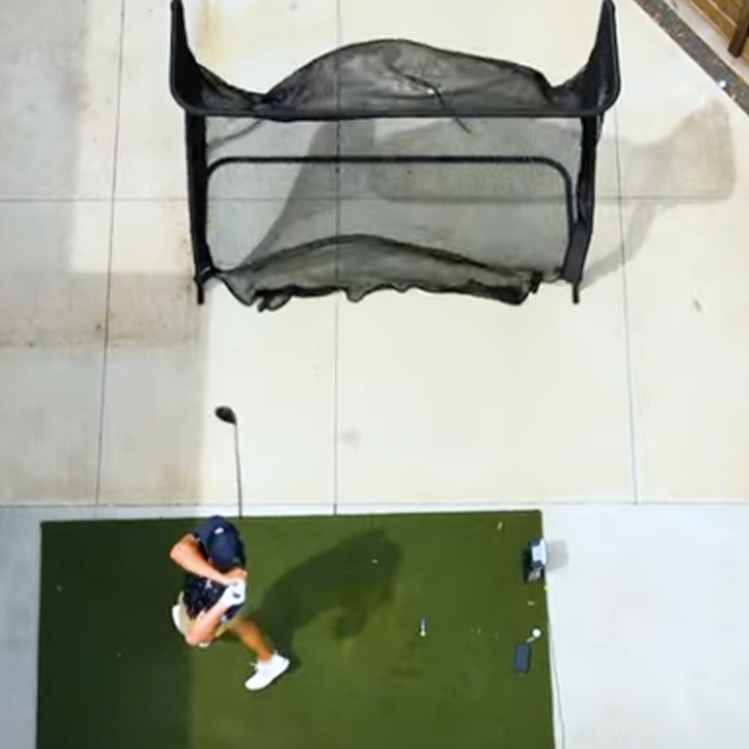 Person swinging a golf club on a green mat with a practice net in front. Overhead view.