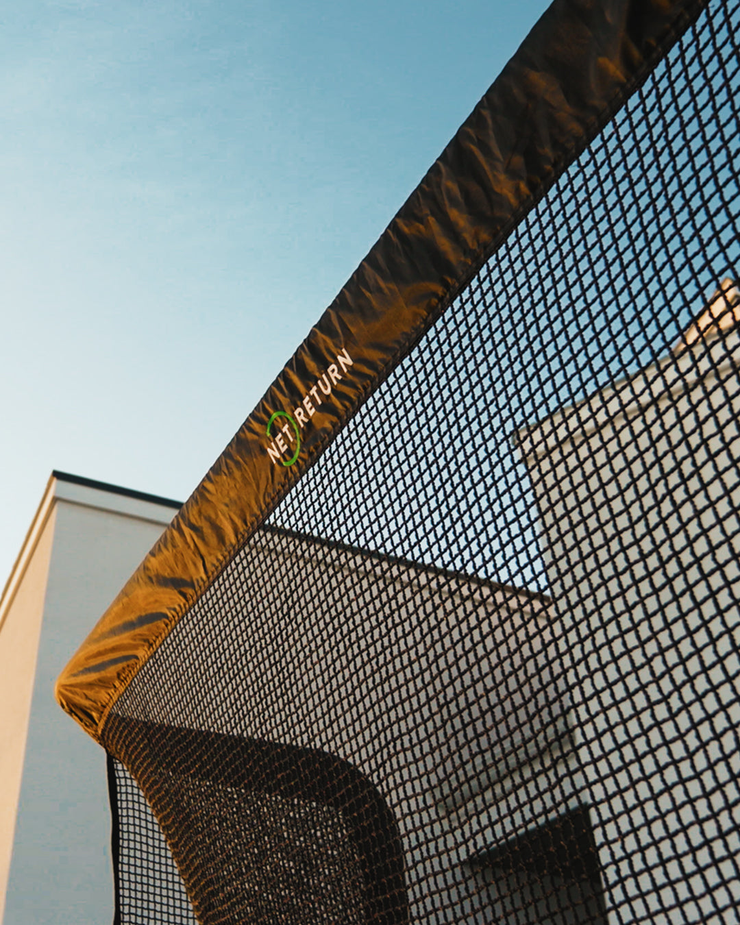 Close-up of a black mesh net with a brown border against a blue sky, featuring a building in the background.