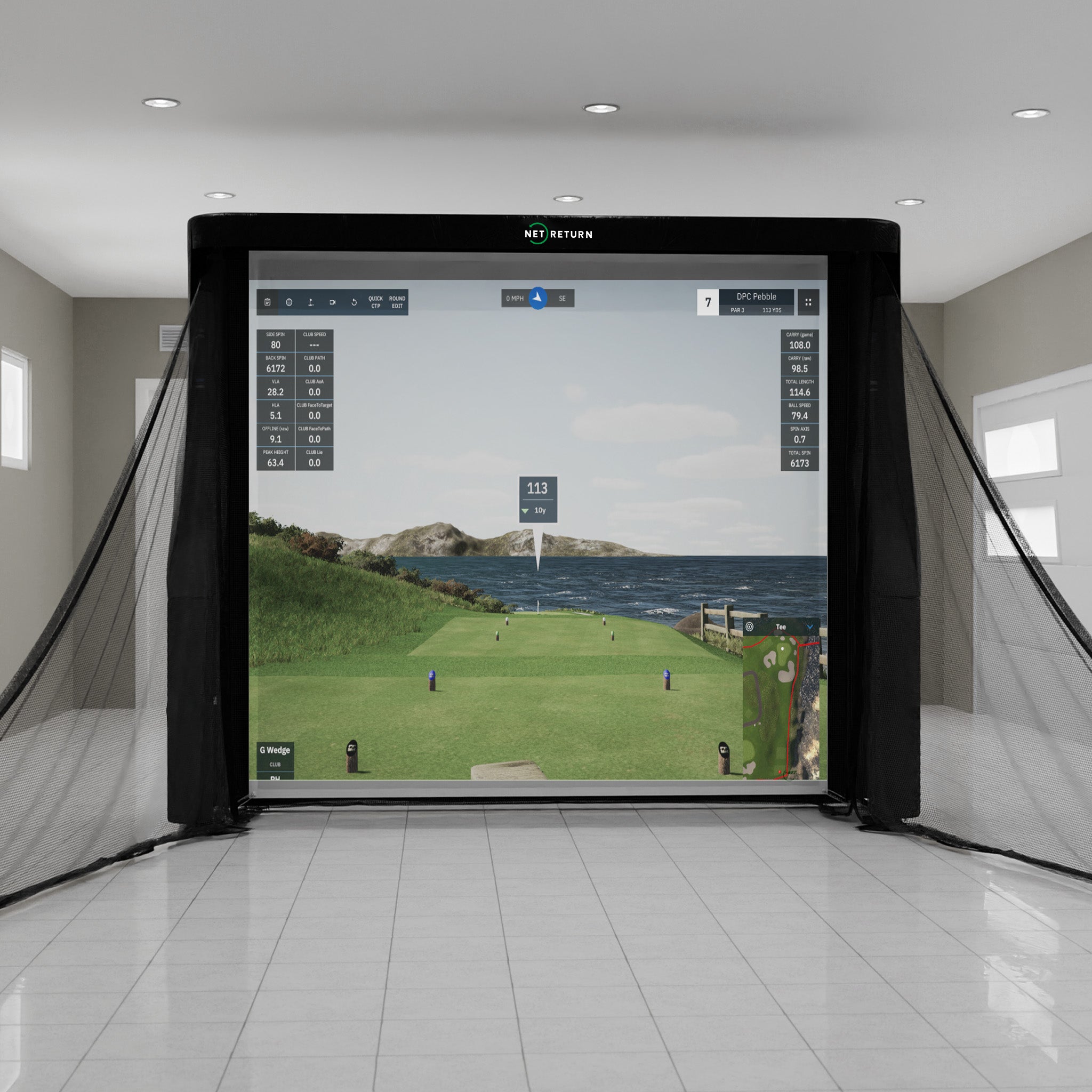 Indoor golf simulator setup with a digital screen displaying a golf course scene, surrounded by protective netting in a bright room.