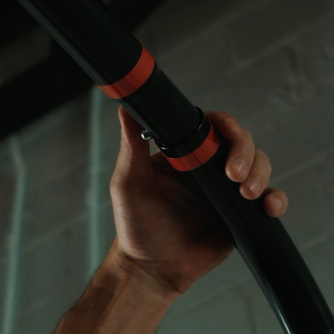 A person's hand grips a black pole with red bands in a dimly lit environment.