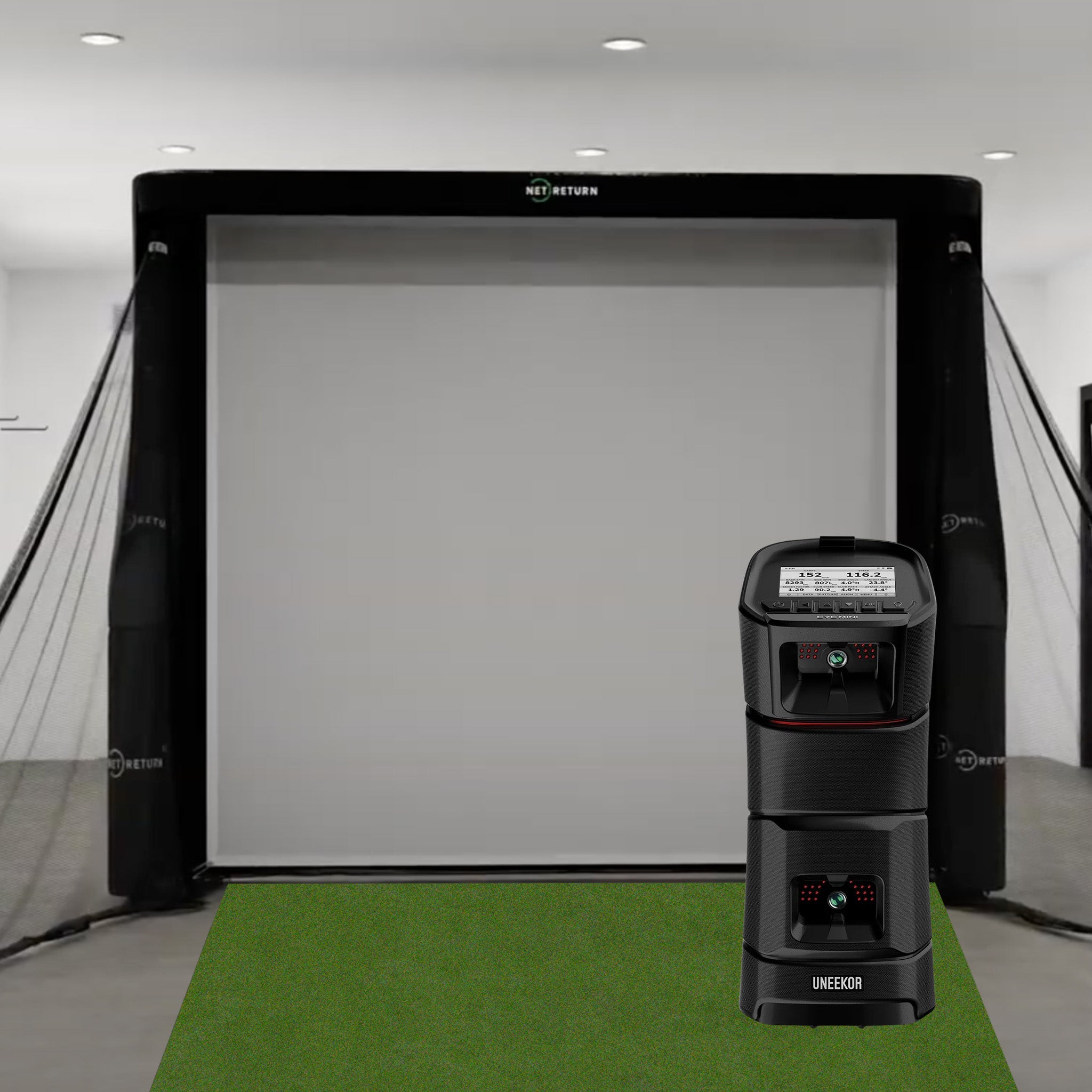 Indoor golf simulator setup with a large screen, netting, and a launch monitor on a green mat.