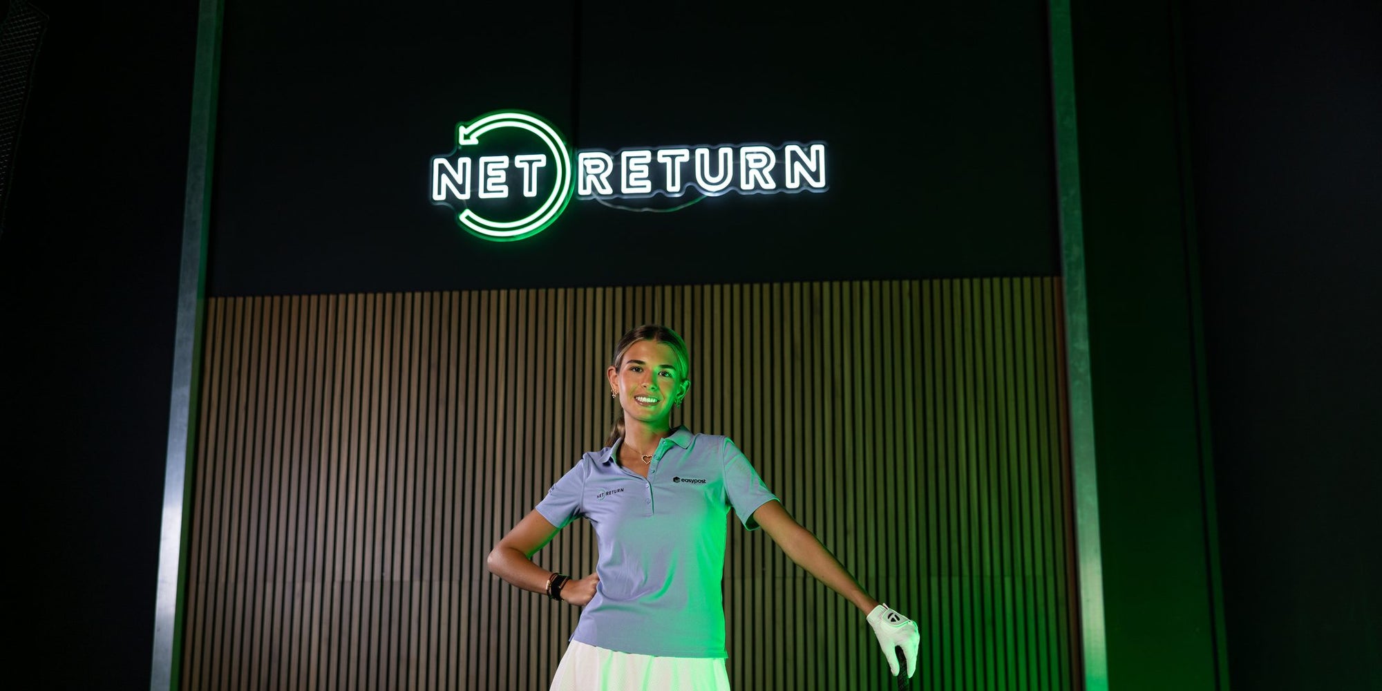 Kai Trump, Net Return athlete, with a golf club in front of the NET RETURN neon sign