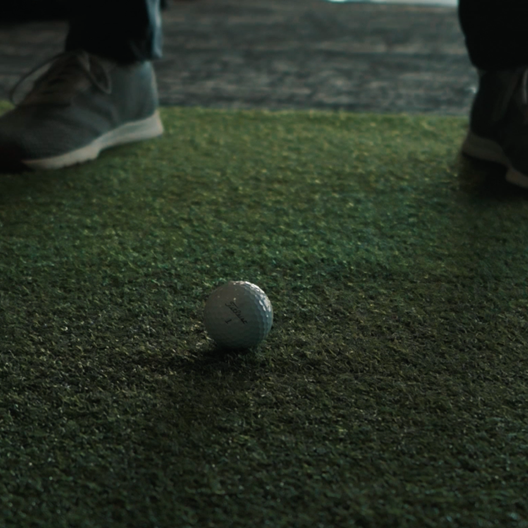 A person standing on artificial turf near a golf ball.