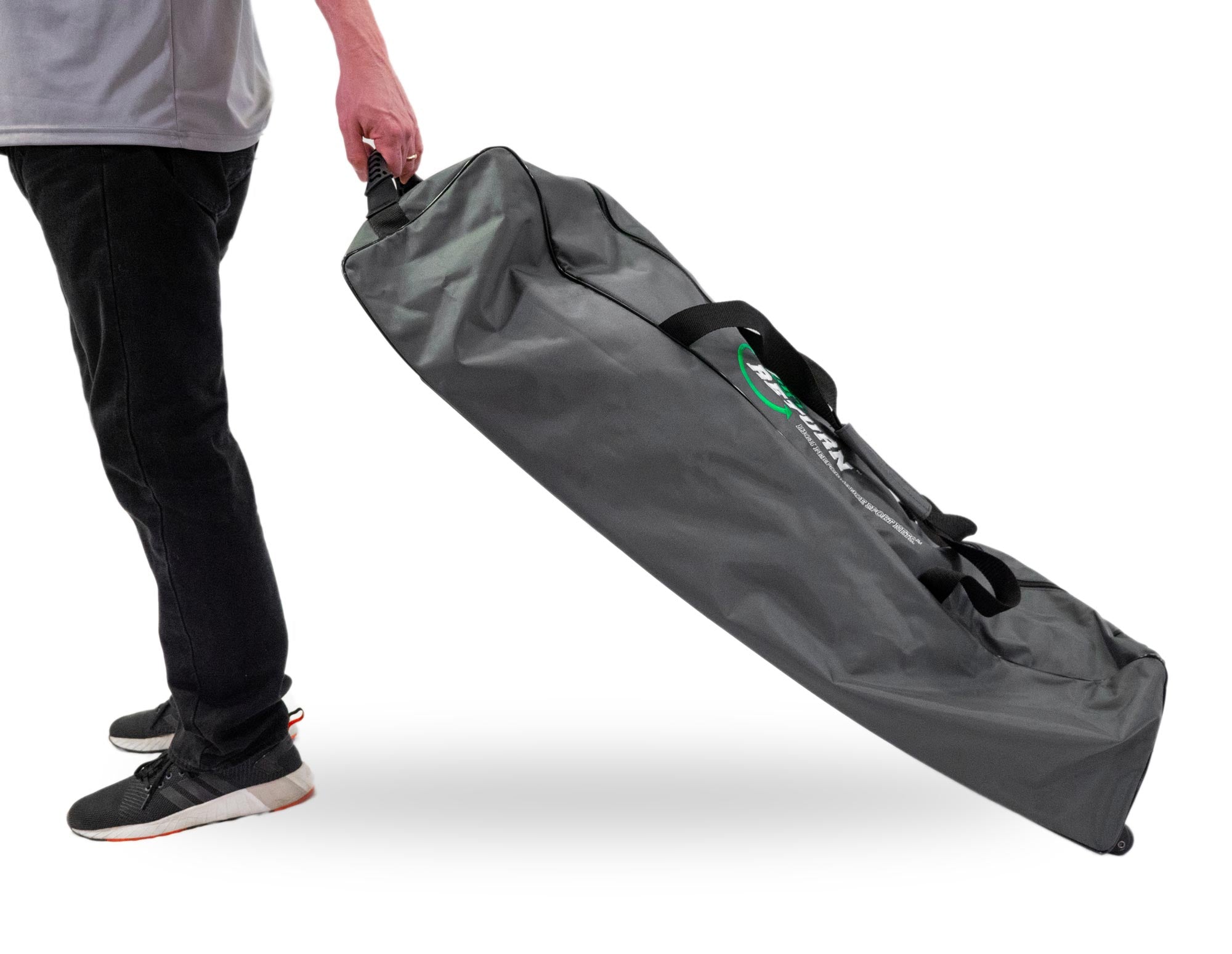 A person carries a large, dark gray bag with a handle, wearing black pants and black sneakers with white soles.
