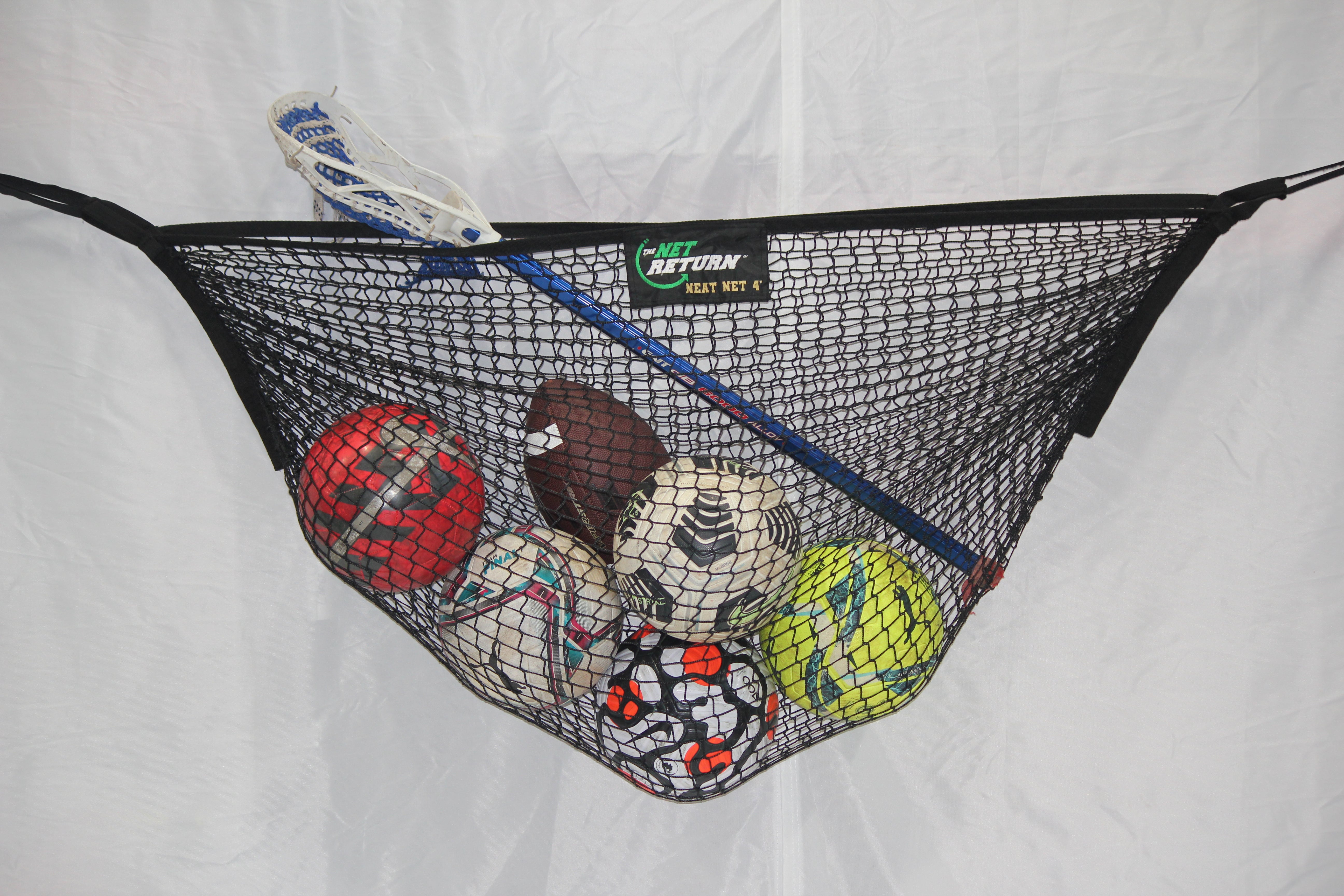 A black net holds various sports balls: a red basketball, a blue lacrosse stick, a brown football, a white soccer ball, a volleyball, and a tennis ball against a white background.