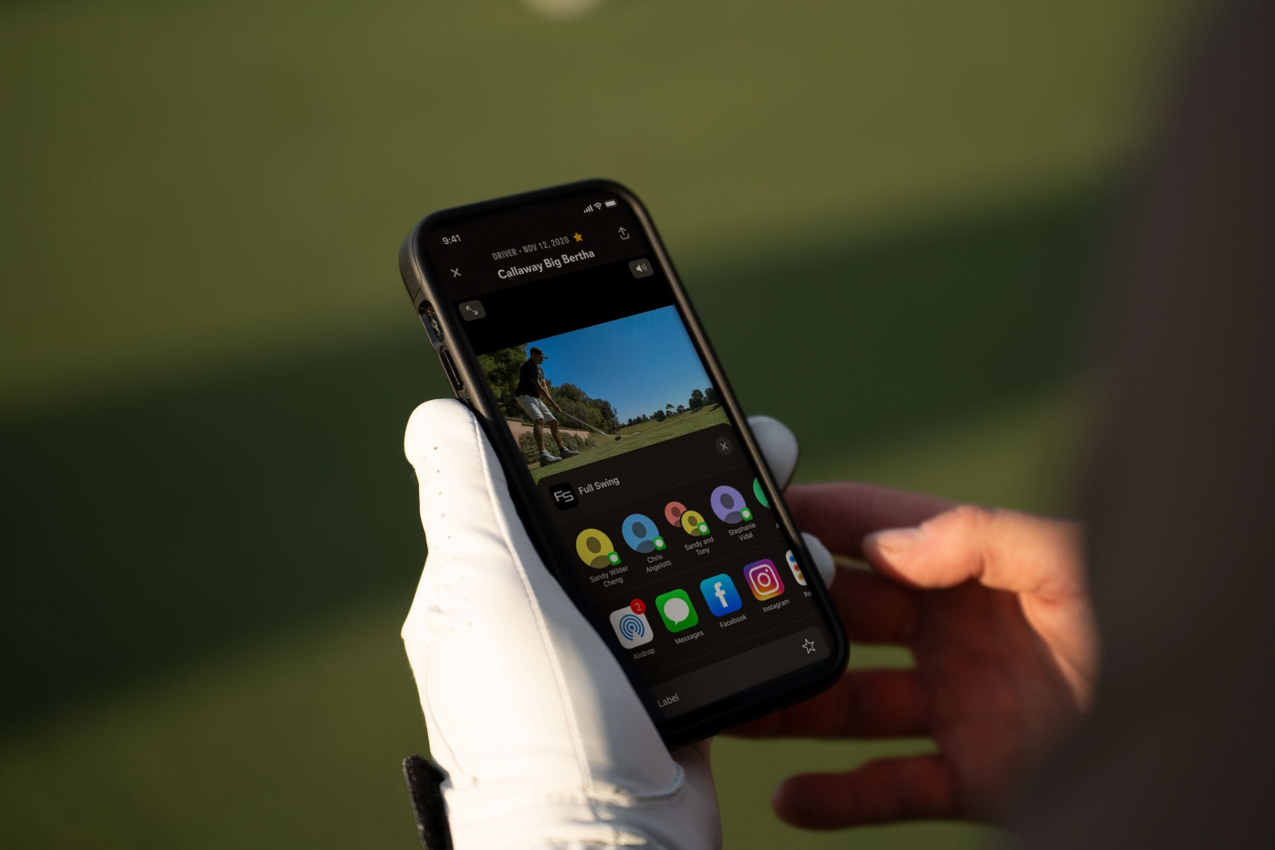 Person wearing a glove holds a smartphone displaying a golf video and various app icons on the screen.