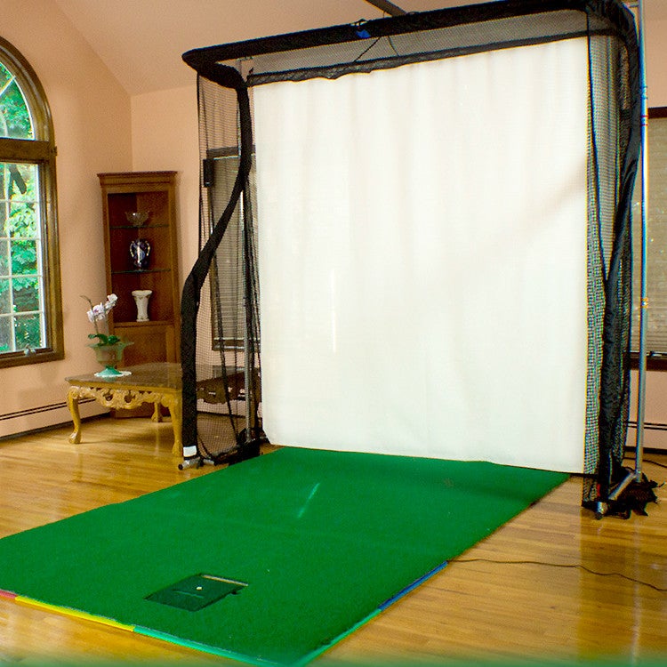 Indoor golf simulator with a net, white projection screen, and green mat. Room has wooden floors, a shelf, and a window.