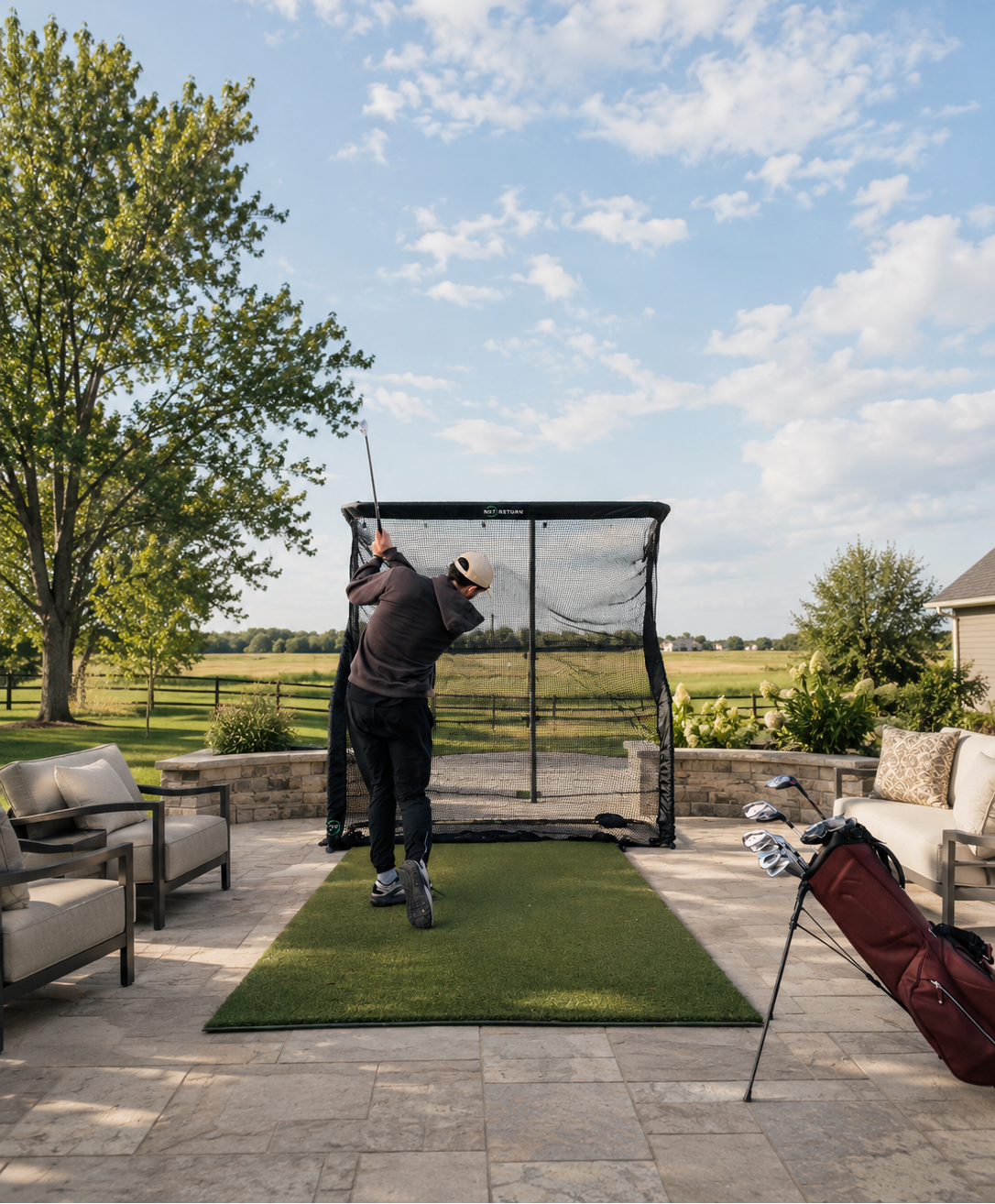 Person practicing golf swings in a backyard with a golf net and green mat.
