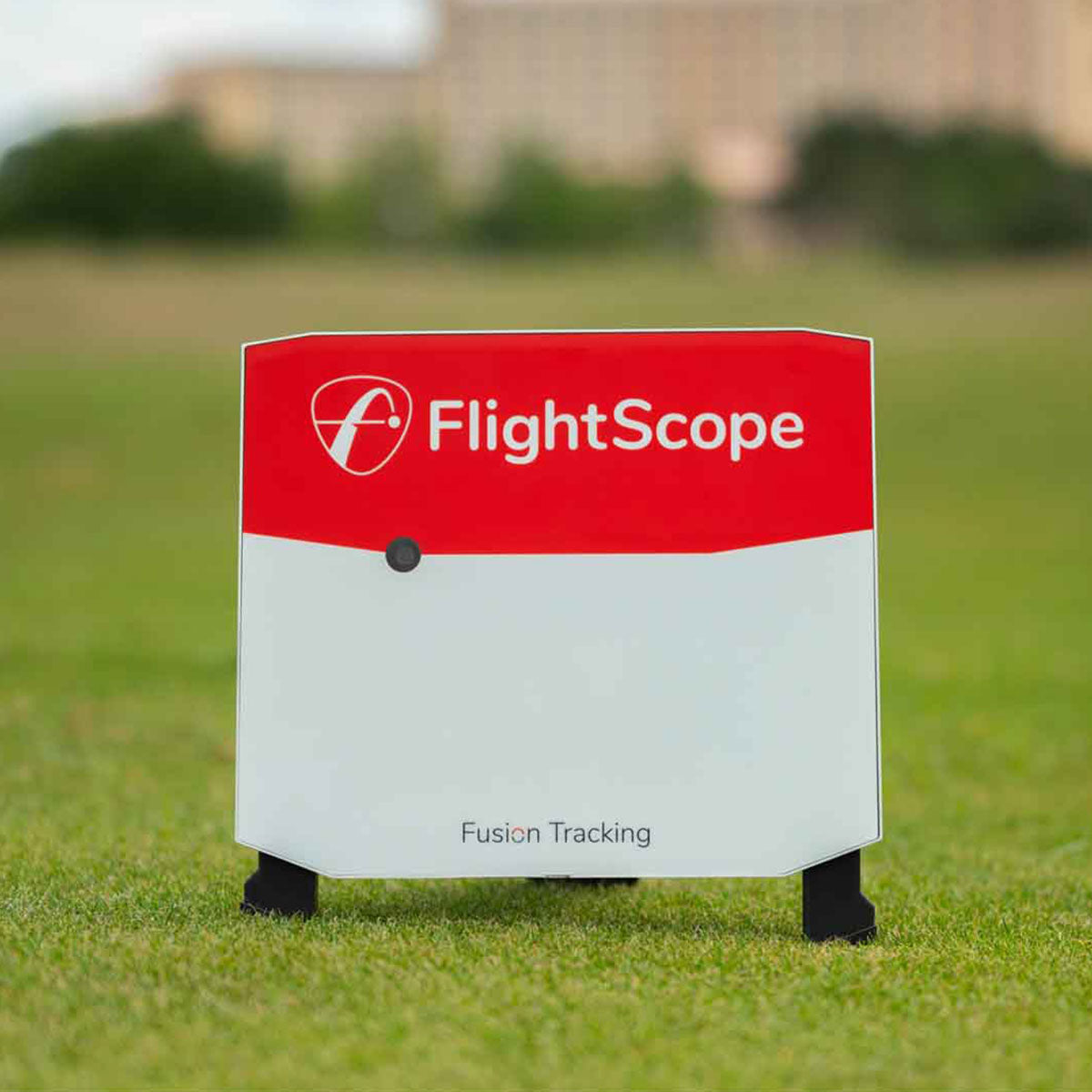 A rectangular FlightScope X3 device with a red and white exterior stands on grass, featuring the advanced Fusion Tracking technology by FlightScope Golf.