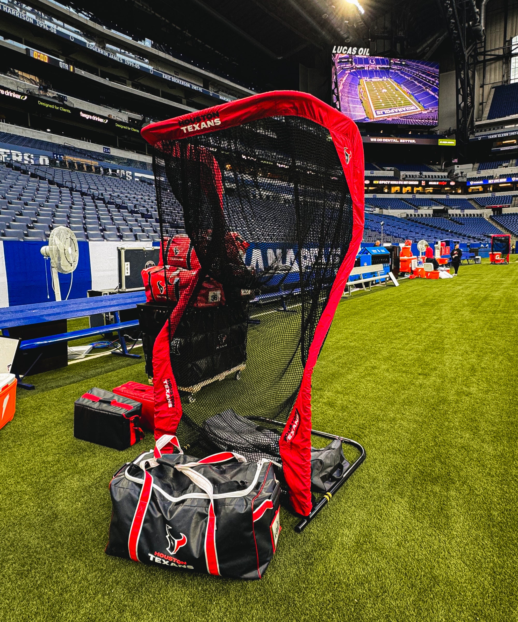Football practice equipment on a field, including a net, bags, and team-branded items in a stadium setting.