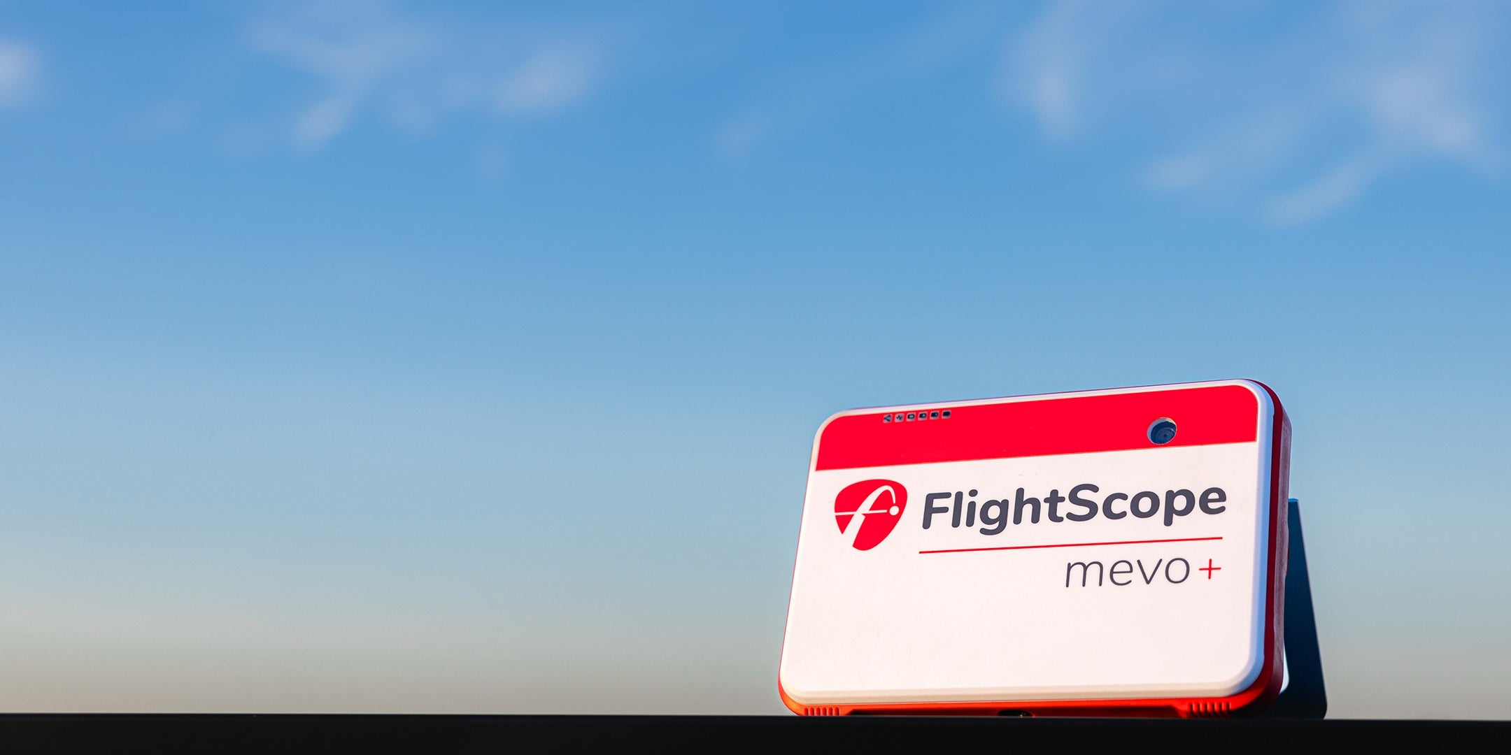 FlightScope Mevo+ device against a clear blue sky background.