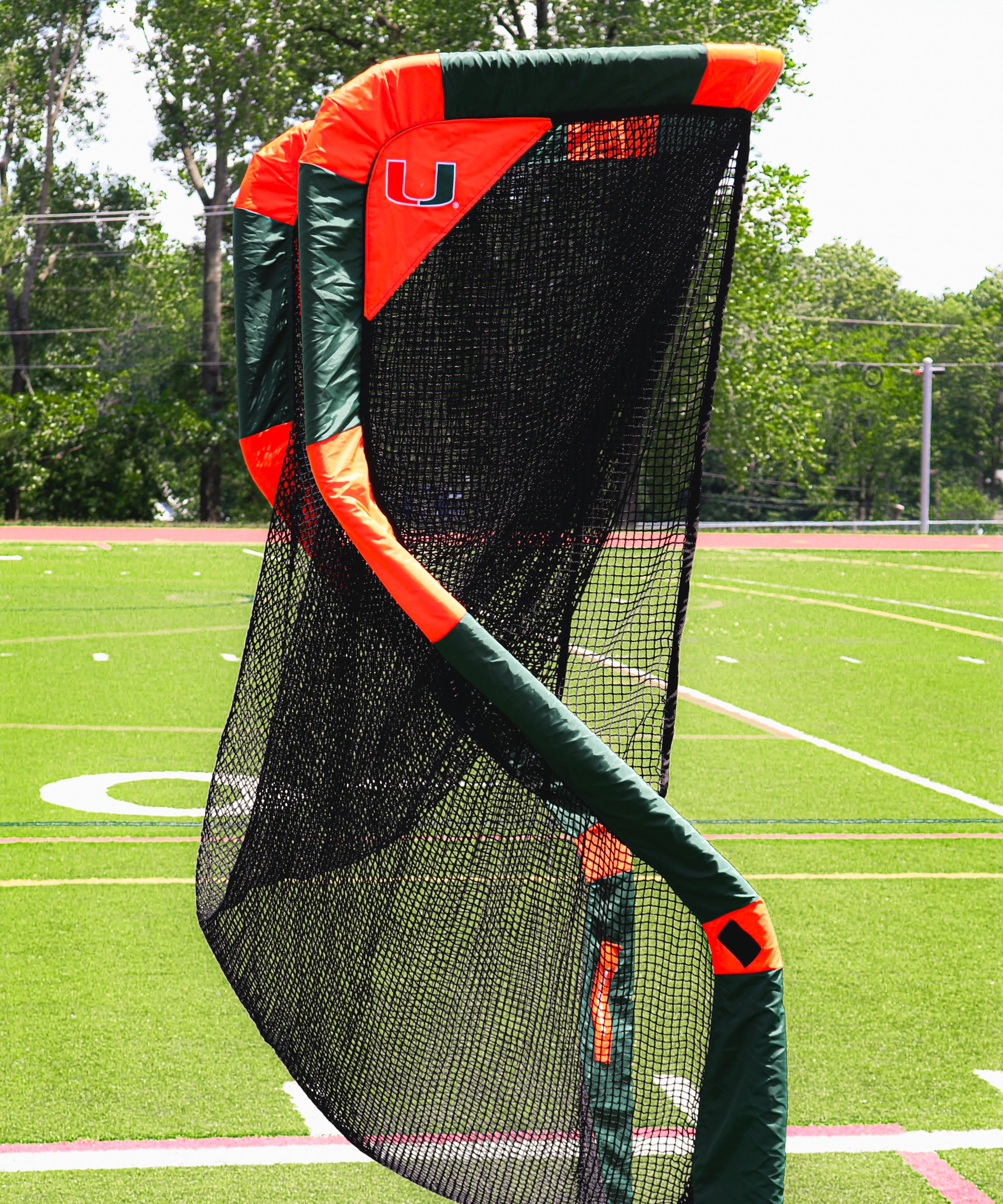 A twisted sports net with green and orange padding stands on an athletic field.