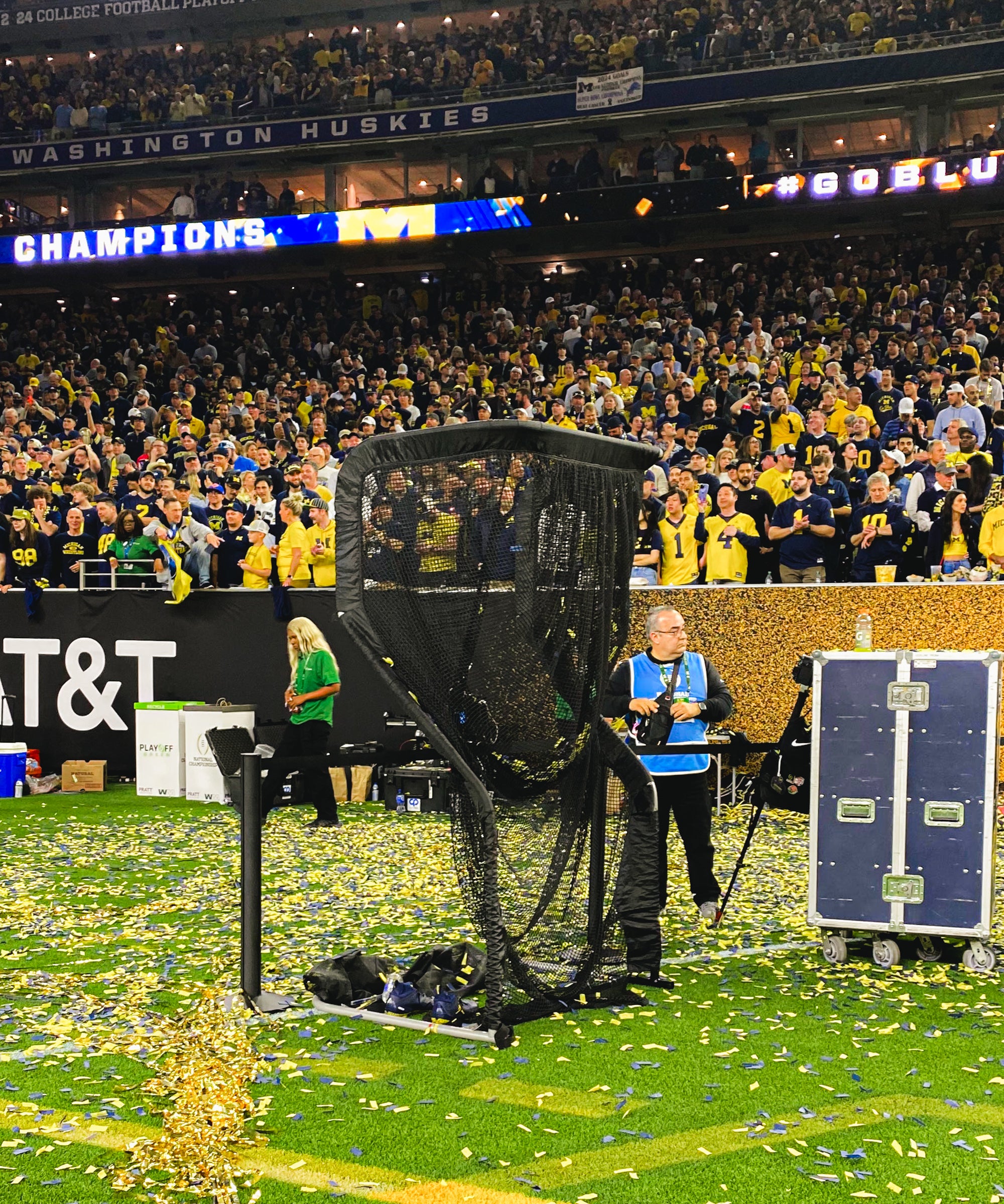 Football field filled with confetti, a large netted camera, and a cheering crowd in the background. "CHAMPIONS" banner is visible.