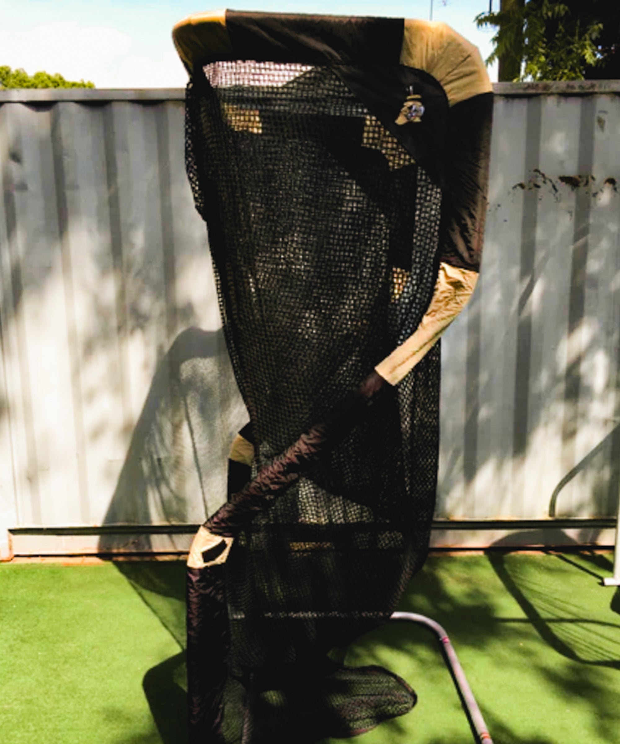 A large net trap set up outdoors on a grassy surface, supported by a metal frame, with a tarp covering the top.
