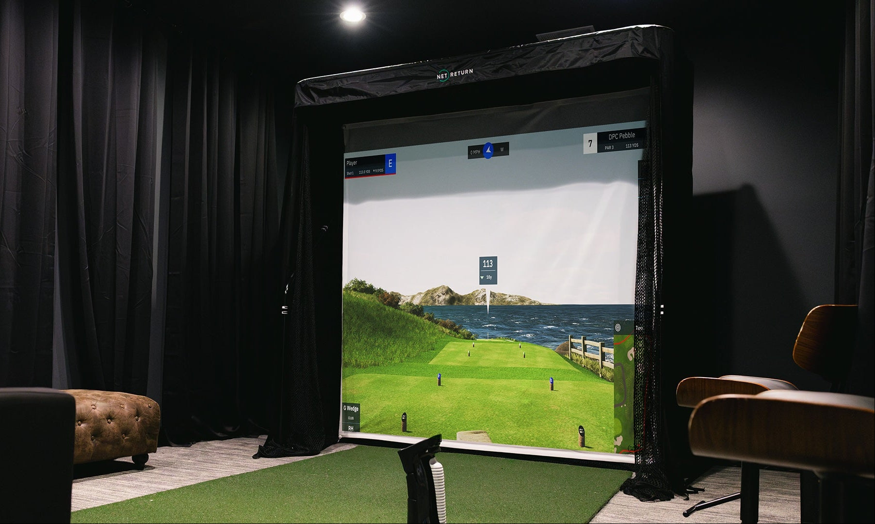A golf simulator setup in a dimly lit room with a large screen displaying a golf course scene.