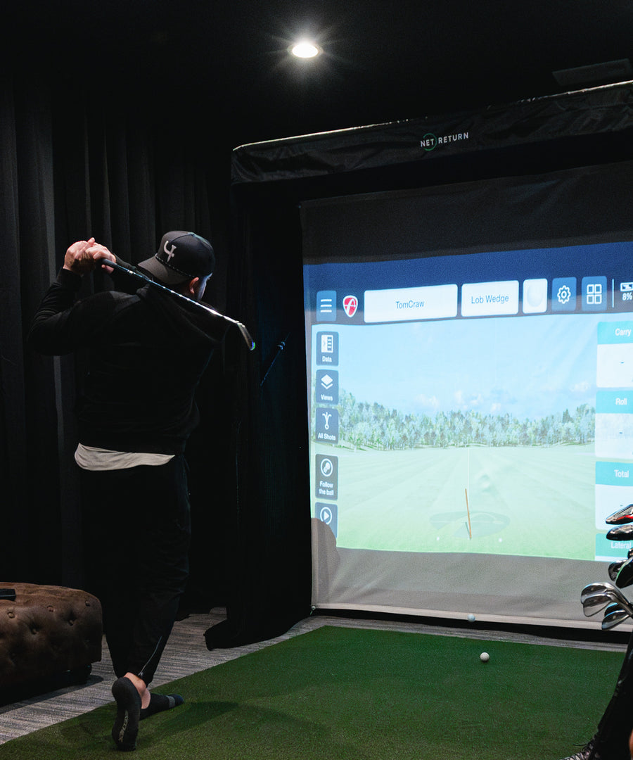Person playing indoor golf with a simulator screen displaying a golf course.