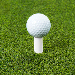 A golf ball placed on a tee on a grassy field.