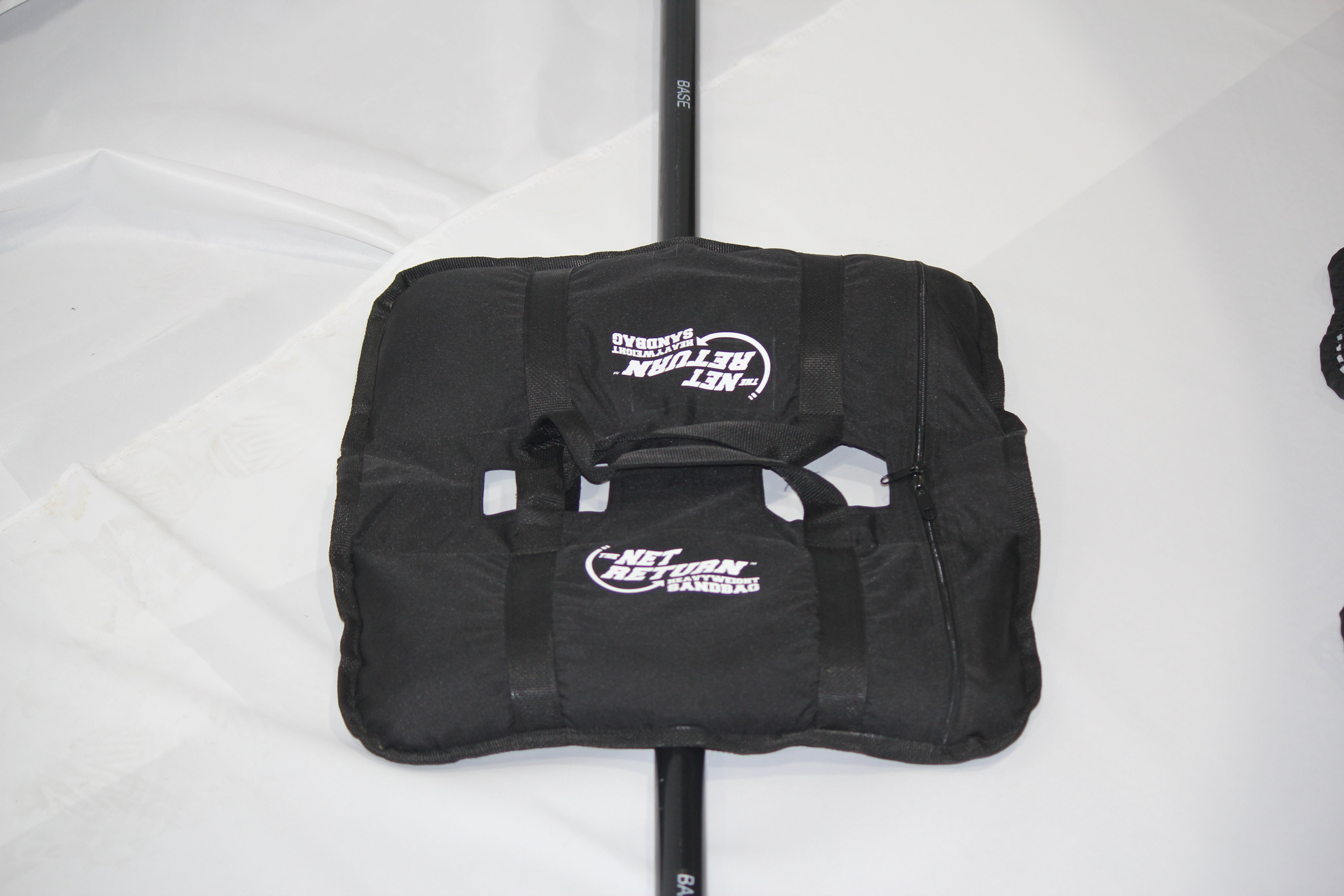 Black Net Return sandbag base weight with white logo, lying on a white surface.