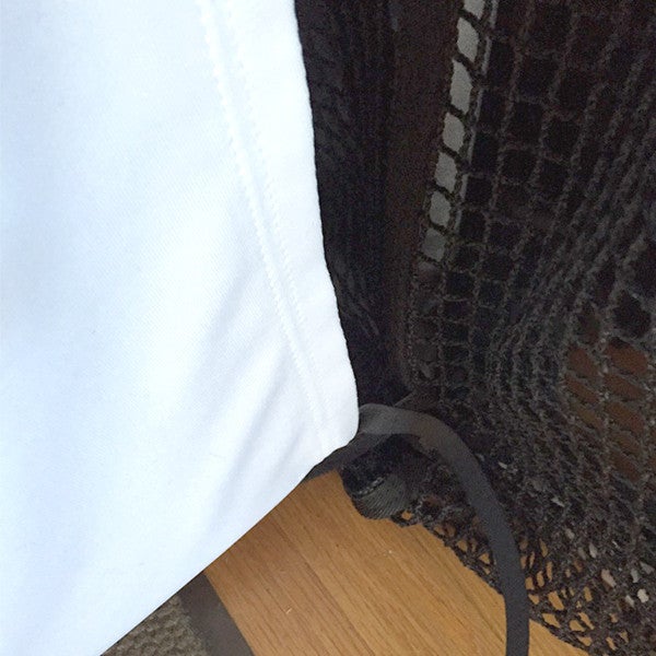 Close-up of a white fabric and a black mesh material overlapping on a wooden surface, with a black strap visible.